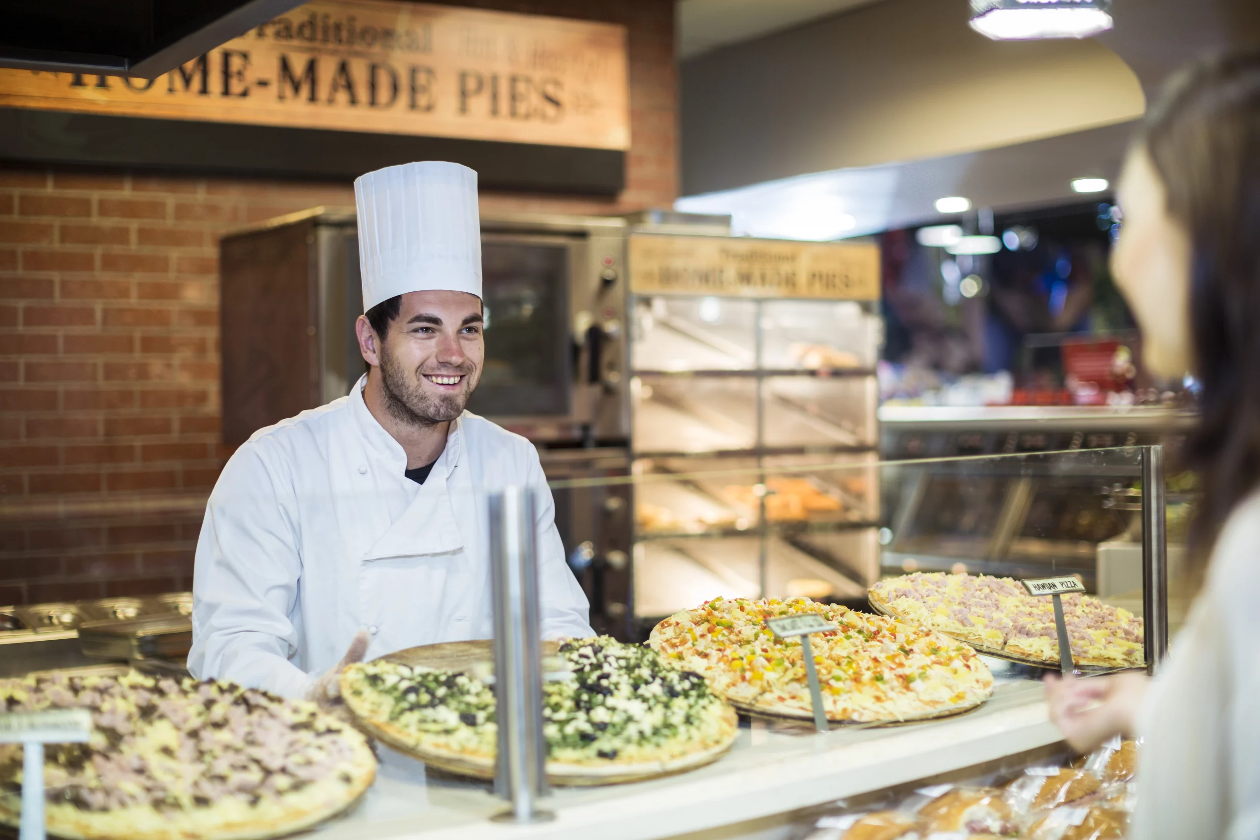 Male chef in bakery serving pizza to female client
